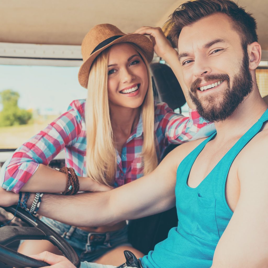 Getting away on weekend. Happy young couple smiling at camera while sitting inside of the minivan Cosmetic Dentistry