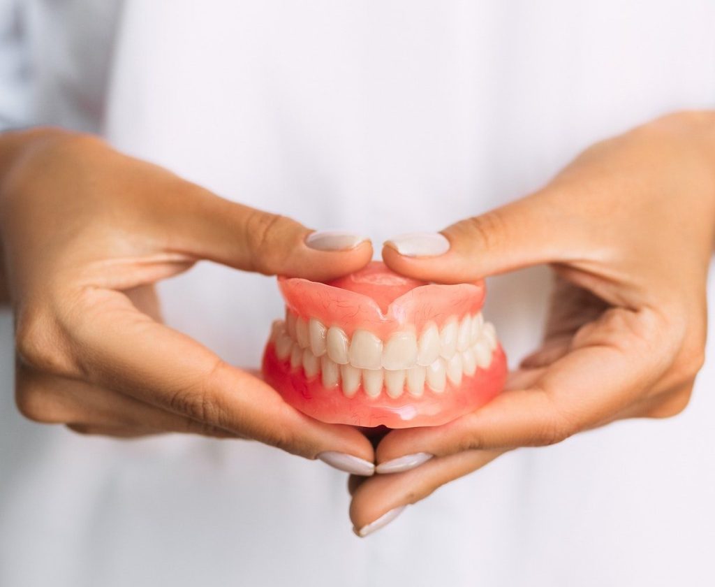The dentist is holding dentures in his hands. Dental prosthesis in the hands of the doctor